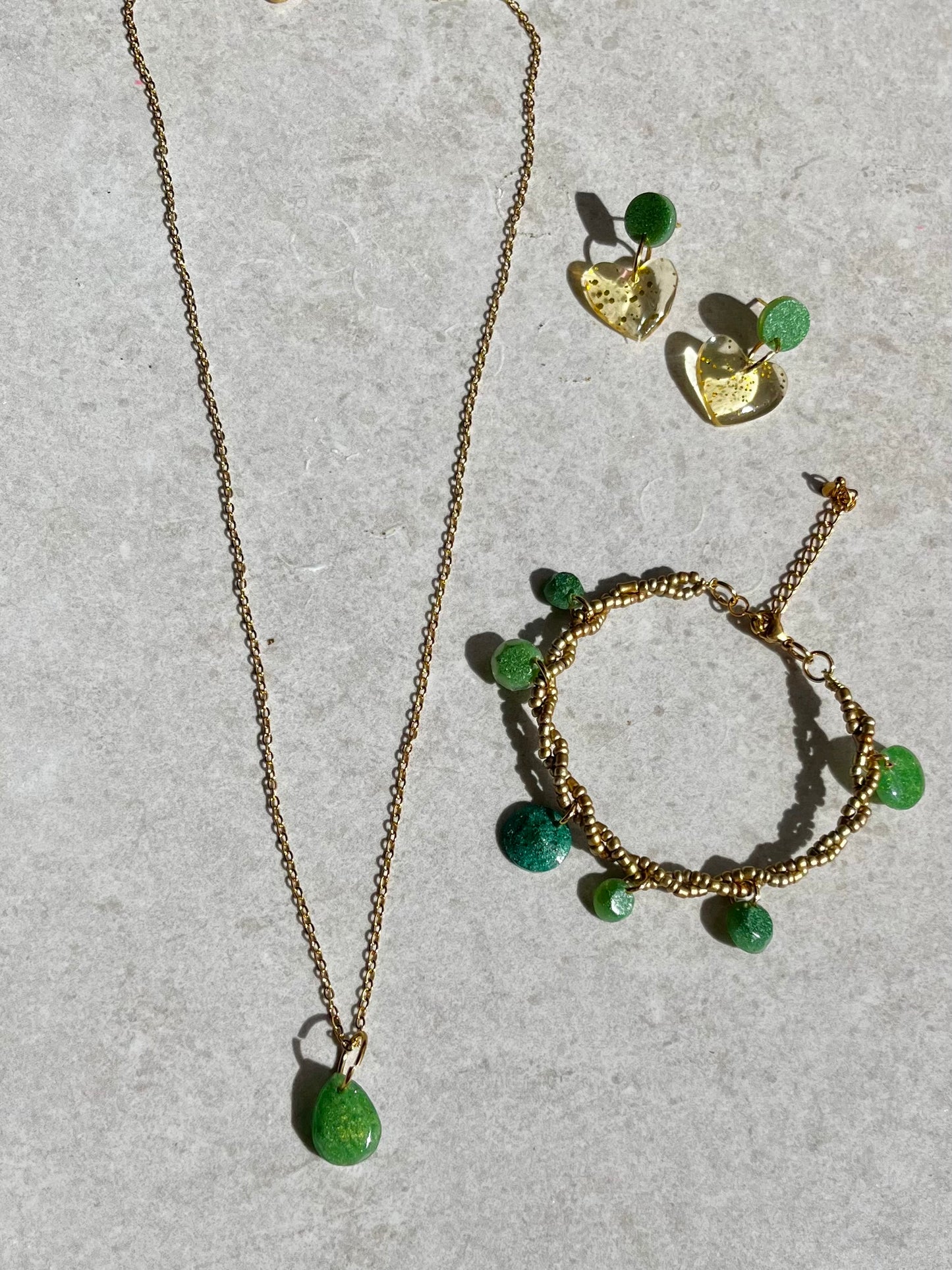 Conjunto de pendientes, collar y pulsera en dorado con accesorios de resina verde.
