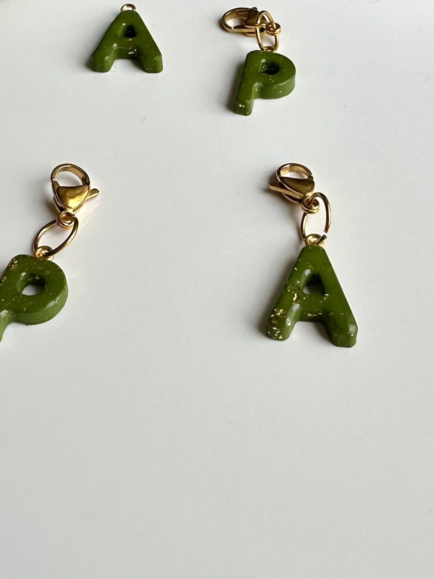 Llavero/colgante con inicial en color verde y toques dorados.