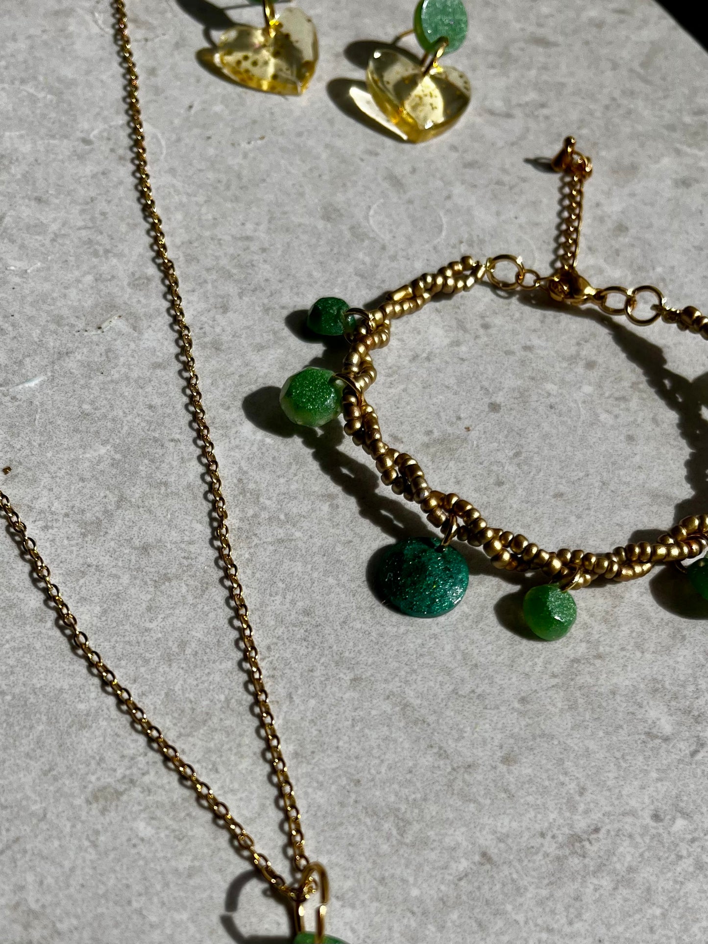 Conjunto de pendientes, collar y pulsera en dorado con accesorios de resina verde.