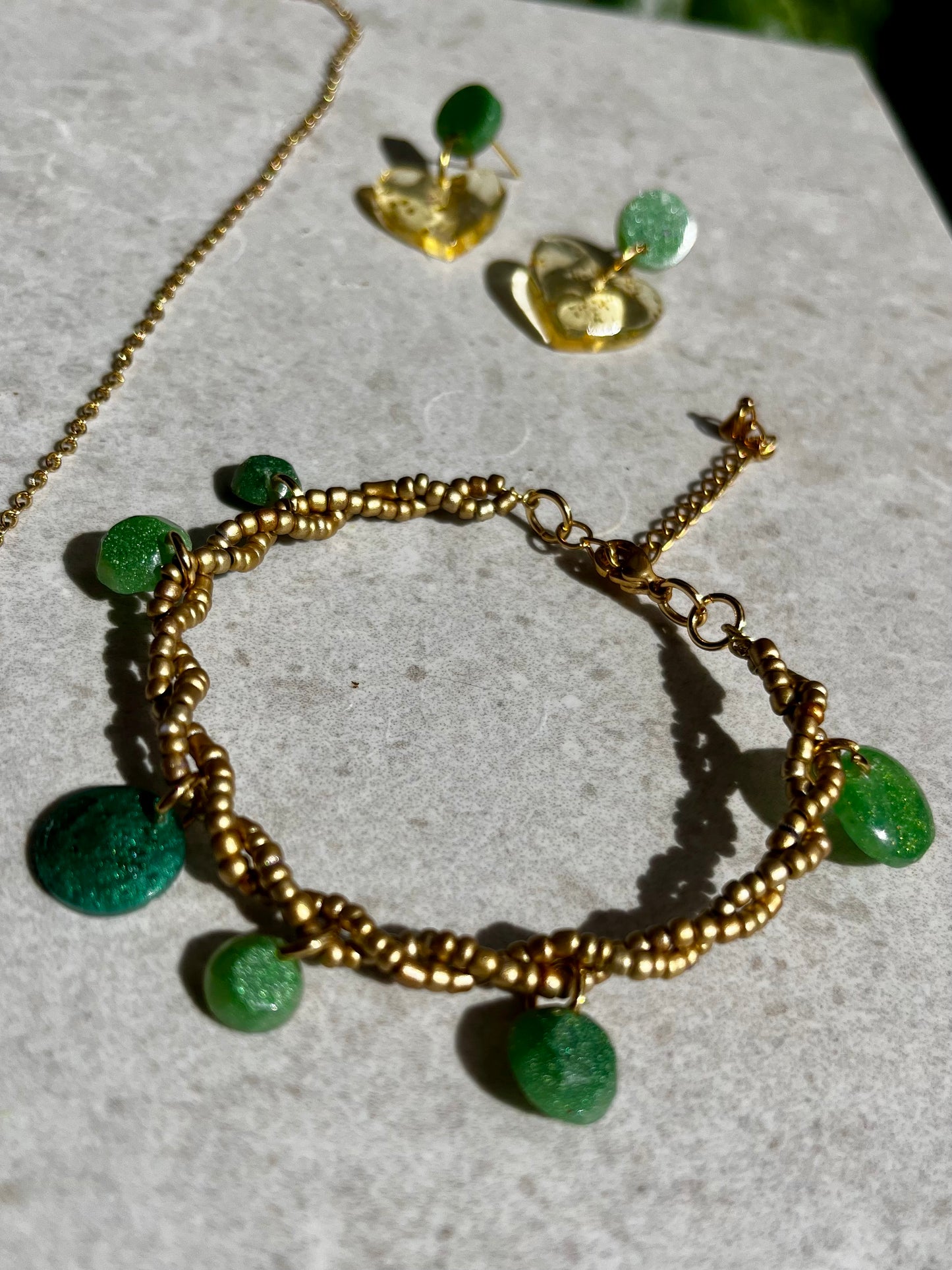 Conjunto de pendientes, collar y pulsera en dorado con accesorios de resina verde.