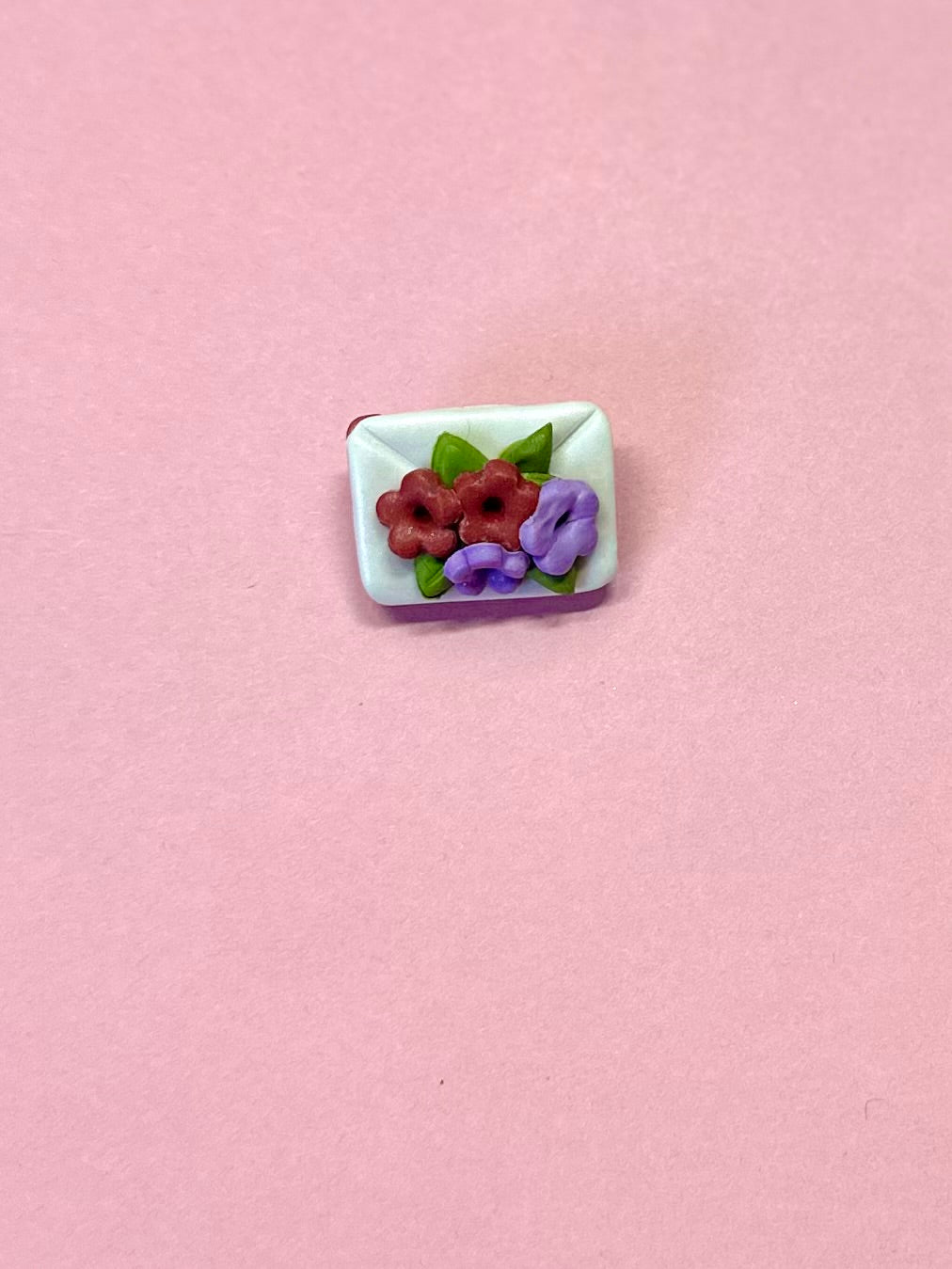 Broche de sobre blanco y flores rojas y lilas.