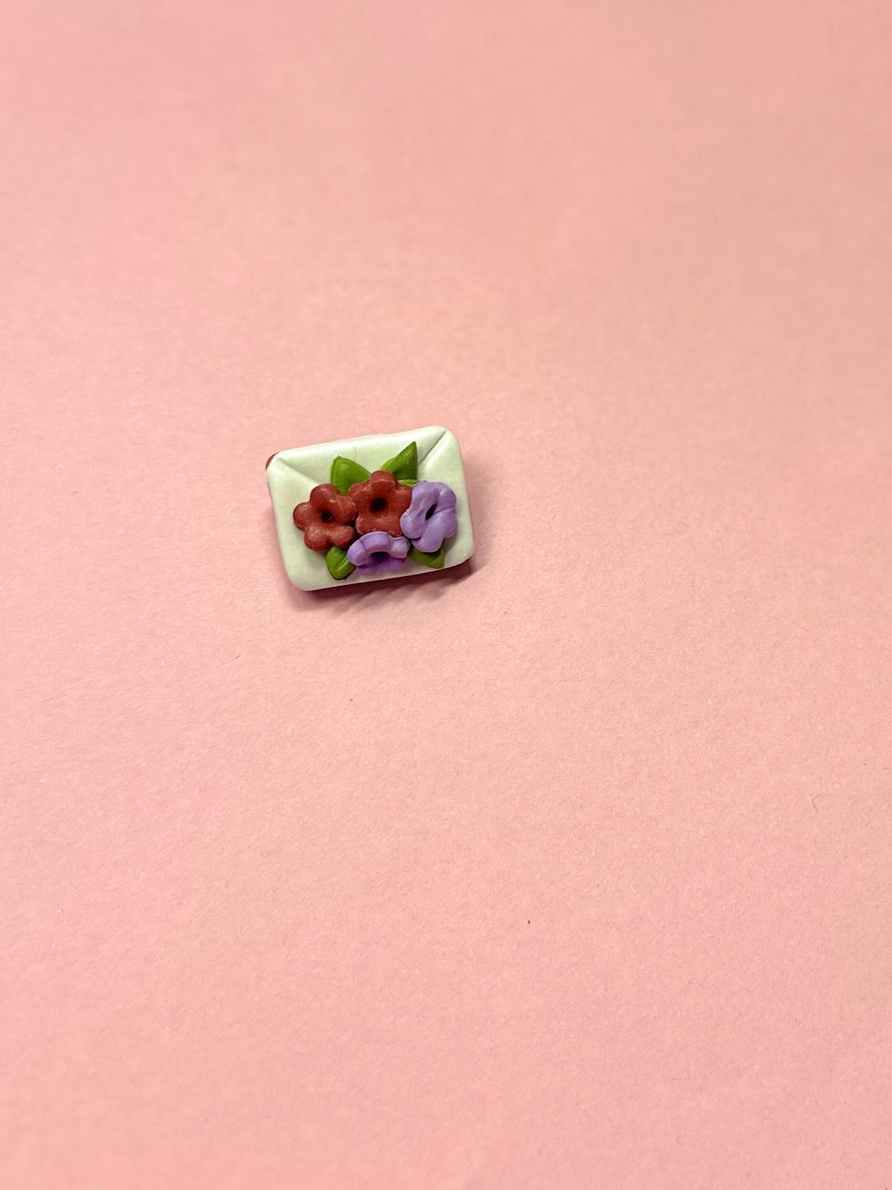 Broche de sobre blanco y flores rojas y lilas.
