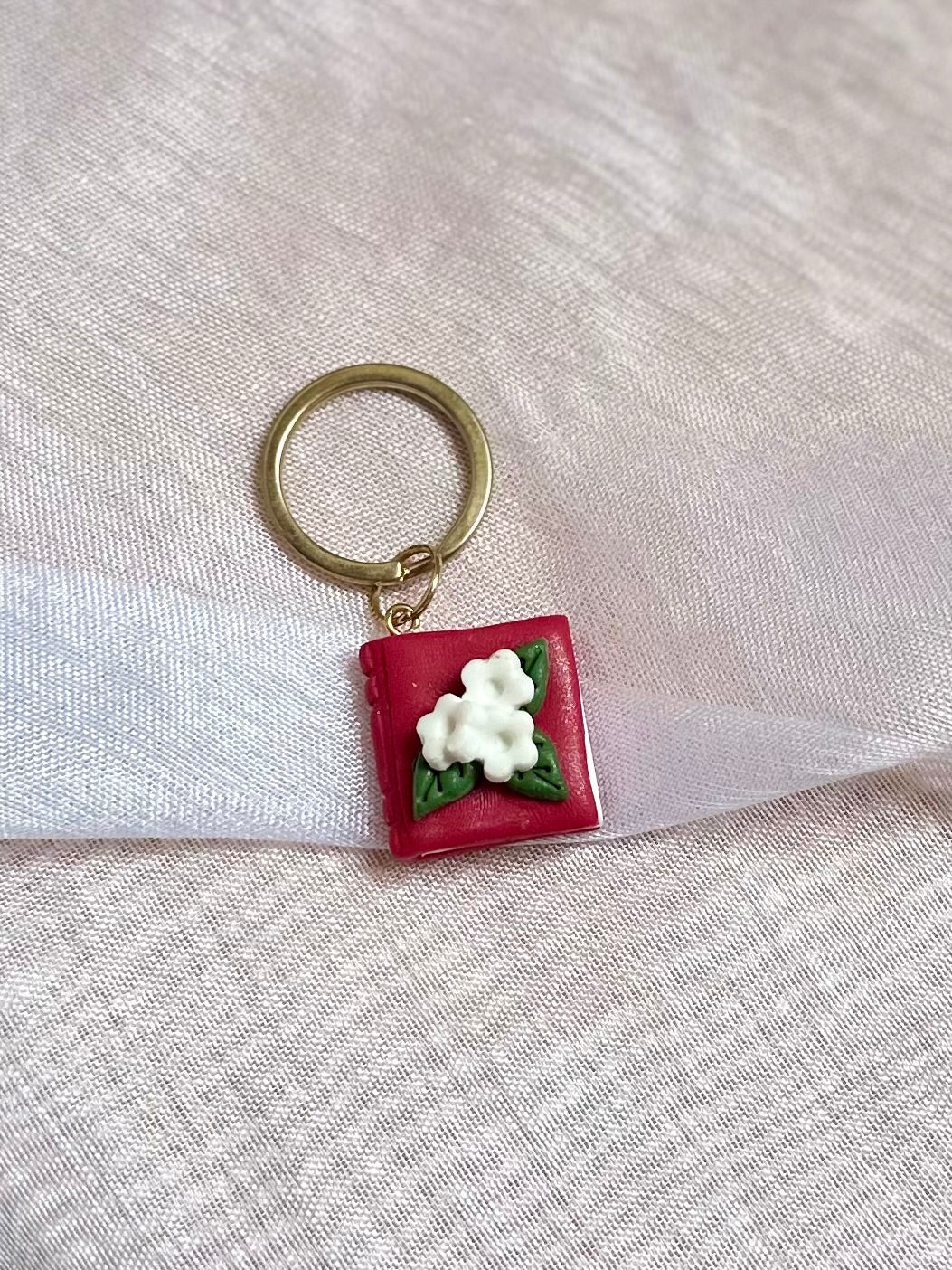 Llavero de libro rojo y flores blancas